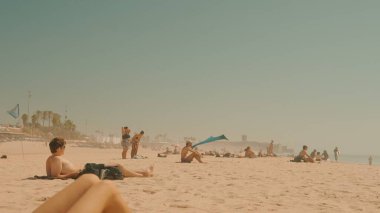 Güneşlenenlerin sıcak havanın ve kumlu sahillerin tadını çıkardıkları huzurlu bir sahil sahnesi.