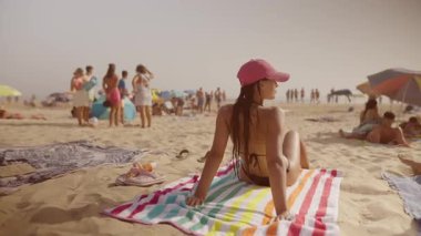 Muhteşem güneşli bir plaj günü. Canlı bir kalabalığın ortasında gevşeyen bir kadının sergilendiği.