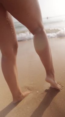 Çıplak ayaklar güneşli sahilde geziniyor, yumuşak sularda yüzüyor ve altındaki yumuşak kumların tadını çıkarıyor.