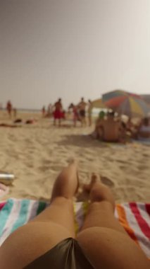 Güneşli bir sahilde güneşli bir günün tadını çıkarın. Güneş banyosu yapanlar ve çeşitli renkli şemsiyelerle.