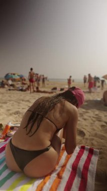 Güneşlenen güneşli bir sahil manzarası. Güneşin sıcaklığının ve parlak bir havlunun üzerindeki kumların tadını çıkarıyor.