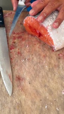 Uzman eller, güzel bir ahşap kesme tahtasındaki taze ve canlı somonları ustalıkla kesiyor.