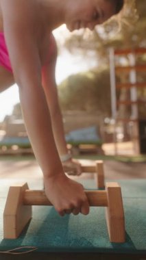 Odaklanmış bir birey güneşin altında ahşap saplı şınav çekiyor, zindelik ve kararlılık gösteriyor..