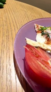 Canlı bir kahvaltı tabağı, taze domatesler, lezzetli yumurtalar, ve mor bir tabakta güzelce sıralanmış otlar.