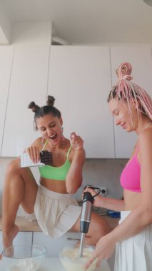 İki arkadaş neşe içinde birlikte yemek pişiriyorlar. Mutluluk ve kahkaha dolu bir mutfakta.