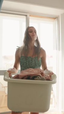 Genç bir kadın bir çamaşır sepetini ustalıkla dengede tutuyor. Renkli, ışıl ışıl kıyafetlerle dolu bir sepet.