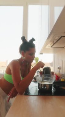 Genç bir kadın parlak mutfağında mutlu bir şekilde yemek pişiriyor. Malzemeleri kasede çırpma makinesiyle ustalıkla karıştırıyor.