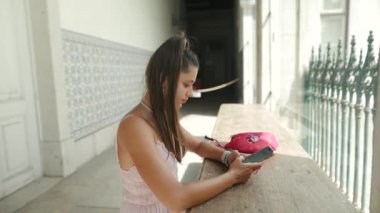 Genç bir kadın modern bir mekanda şık bir masada otururken akıllı telefonuyla mutlu mesut iletişim kuruyor.