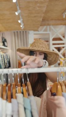 Şık bir kadın neşeli bir şekilde canlı bir mağazada şık kıyafetlere göz atar. Güzellik saçar ve bu deneyimden zevk alır.