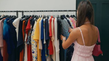 Bir kadın coşkuyla çeşitli moda tercihlerini gösteren canlı bir elbise rafını keşfediyor.