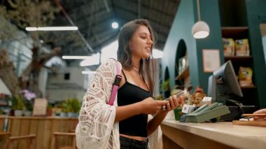 Genç bir kadın, modern yaşam tarzını ve ambiyansı sergileyen bir kafede para ödüyor.