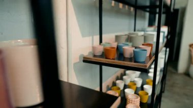 Raflarda güzel bir şekilde seramik bardaklar ve dekoratif kaplar güzel bir şekilde dizilmiş.