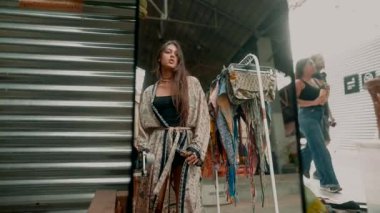 Şık bir model, bir pazarın canlı atmosferinde bir dizi modaya uygun kıyafet sergiliyor.