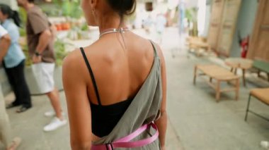 Tarz sahibi bir kadın, insanlarla dolu ve yemyeşil bir ortamda gezer.