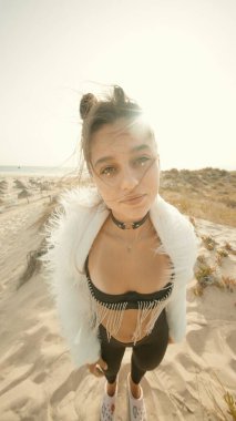 Şık bir birey kumsalda güven içinde poz veriyor, çağdaş moda ve rahat yaz atmosferleri sergiliyor.