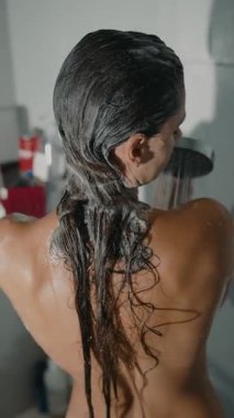 Duşta, bir kadın en sevdiği şampuanı nazikçe sürüyor, sakin ve sakin bir banyo rutini sergiliyor.