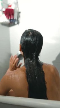 Dinlenen ve rahatlatıcı bir banyo deneyiminin keyfini çıkaran bir kadın aynı zamanda uzun ve pürüzsüz saçlarıyla da ilgilenir.
