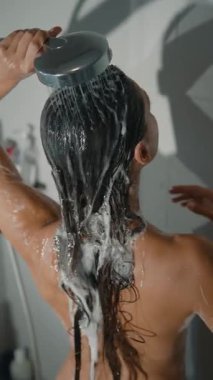 Bir kadın uzun, ıslak saçlarına ustalıkla şampuan sürerek ferahlatıcı bir duştan büyük zevk alır.