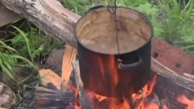 Ateş yanıyor, bir tencere kaynar su ateşin üzerine asılmış ve yemek hazırlanıyor..
