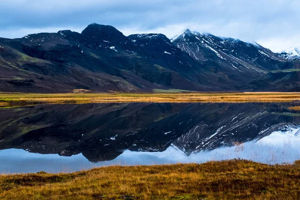 a snowy mountain is reflected in a lake of Islanadia shortly after sunrise