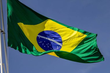 Arka planda mavi bir gökyüzü dalgalanan bir Brezilya bayrağı.