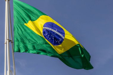 Arka planda mavi bir gökyüzü dalgalanan bir Brezilya bayrağı.