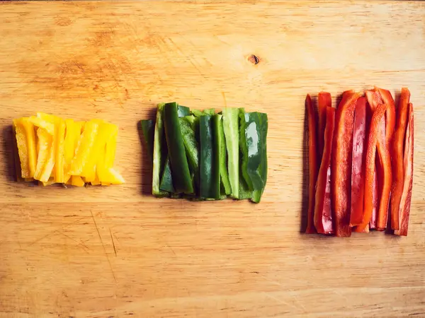 Kırmızı biber, yeşil biber ve ahşap masada sarı biber.