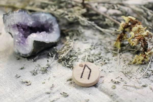 Scandinavian wooden rune Uruz on a homespun linen cloth with amethyst and dried flower.