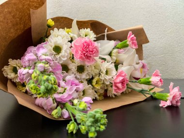 Bir buket narin pembe ve beyaz çiçek siyah bir masada, eko kağıtta..