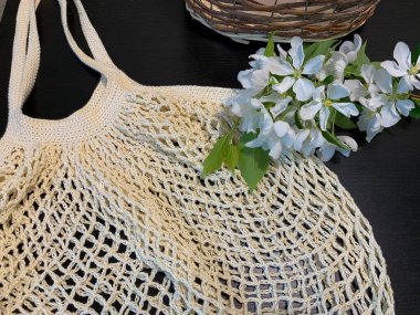 Siyah masada bir torba, sepet ve çiçekler var. Yukarıdan manzara. Plastiksiz kavram.