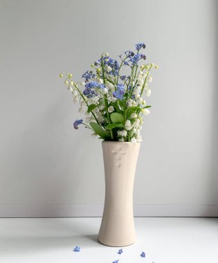 Vadi zambakları ve vazodaki beyaz arka planda mavi çiçekler. Bahar çiçekleri. Sevdiklerine bir hediye..