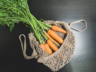 Siyah arka planda, çevre dostu bir ağ torbasının içinde bir avuç havuç. Sıfır atık, sadece sağlıklı yiyecekler, vejetaryenlik