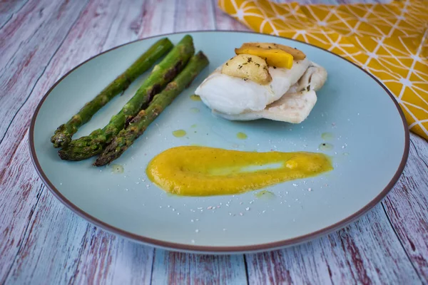 Mango soslu hake fileto ve kuşkonmaz. Sıcak renklerde ve sarı arkaplanlı bir tabak. Deniz ürünleri yemeği.