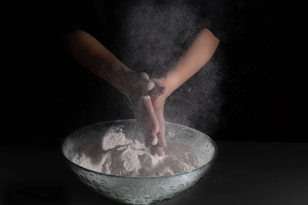 Kadının elleri siyah arka planda un ile alkış tutuyor.