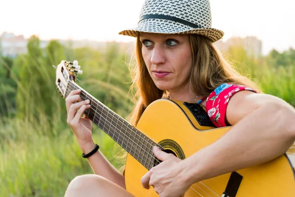 Sarışın, şapkalı ve gitar çalan bir kadının yakın çekimi.
