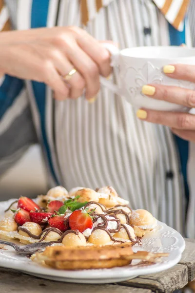 Çay içen ve çilekli ve çikolatalı waffle yiyen bir kadın.