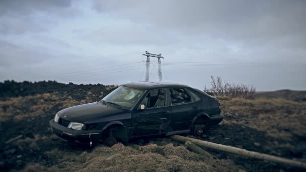 Carro destruído em campo rochoso sob linhas de energia e céu nublado nostálgico — Vídeo de Stock