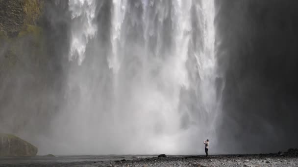 Человек фотографирует водопад Скогафосс в Исландии. — стоковое видео