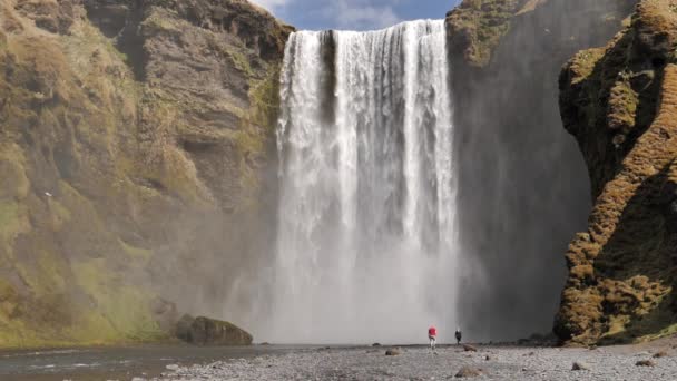 Man and woman walking under Skogafoss waterfall Iceland slow motion — Stock Video