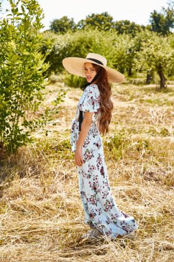 Seksi güzel genç kadın moda modeli giyim uzun mavi şık elbise yaz koleksiyonu aksesuar hasır şapka sıcak doğa Garden yürümek kuru ot romantizm güzel yüzü uzun esmer saç tan güneş.
