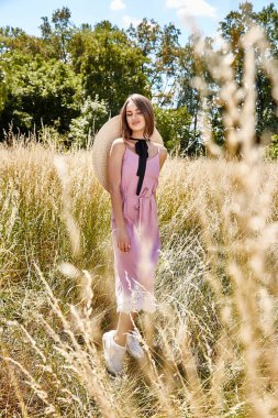 Güzel genç seksi kadın uzun saçları parlak makyaj doğa arka plan manzara kuru spike çim ve ağaç bahçe Yaz modeli pamuk elbise aksesuar hasır şapka güneş gözlüğü moda tarzı giyinmiş.