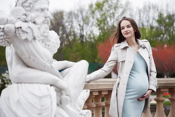 美丽的年轻孕妇一个新生儿九月的怀孕散步在公园秋天的天气穿着薄的浅蓝色礼服和斗篷举行对腹部心脏妈妈健康幸福 — 图库照片
