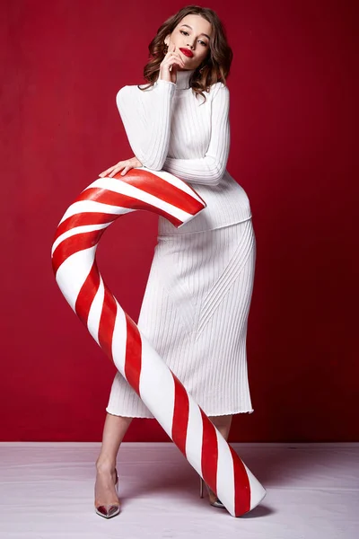 セクシーなかなりの女性ファッション モデル美人スタイル スキニー ニット白ドレスお祝い幸せな休日メリー クリスマスイブ新年パーティー ホールド キャンディ キャラメル杖ブルネットの化粧 — ストック写真