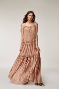 Güzel bir kadın. Makyaj modeli, esmer, mükemmel vücut şekli, bronzlaşmış ten, yaz kıyafetleri, organik uzun bej ipekten elbiseler, şık ayakkabılar, aksesuar takı küpeleri..