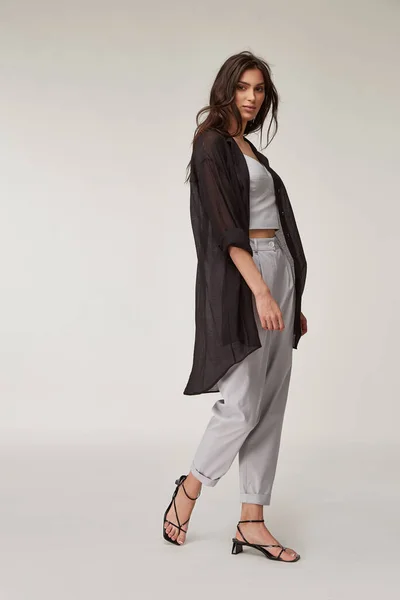 Fashion pretty woman beautiful makeup perfect body shape tanned skin wear clothes summer collection organic textile black cotton cape, light gray suit crop top and trousers stylish sandals shoes.