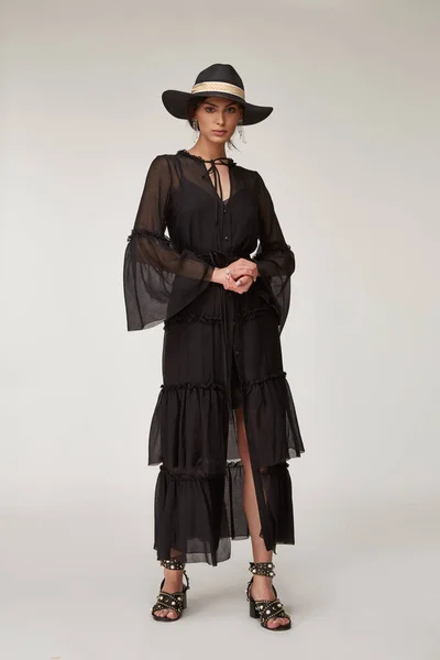 Fashion pretty woman beautiful makeup perfect body shape tan skin wear clothes summer collection organic black cotton cape, silk short dress stylish sandals shoes, accessory hat and jewelry earrings.