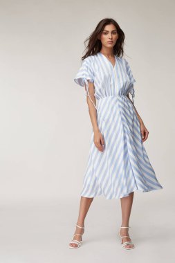 Seksi manken güzel kadın, güzel yüz makyajı, bronzlaşmış vücut, yaz koleksiyonu kıyafetleri, romantik randevu için günlük moda açık ipek, beyaz mavi çizgili uzun elbise..