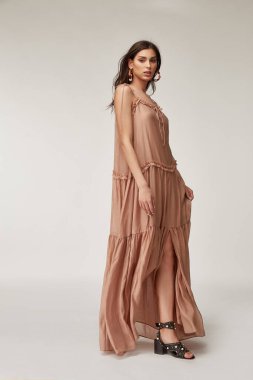 Güzel bir kadın. Makyaj modeli, esmer, mükemmel vücut şekli, bronzlaşmış ten, yaz kıyafetleri, organik uzun bej ipekten elbiseler, şık ayakkabılar, aksesuar takı küpeleri..