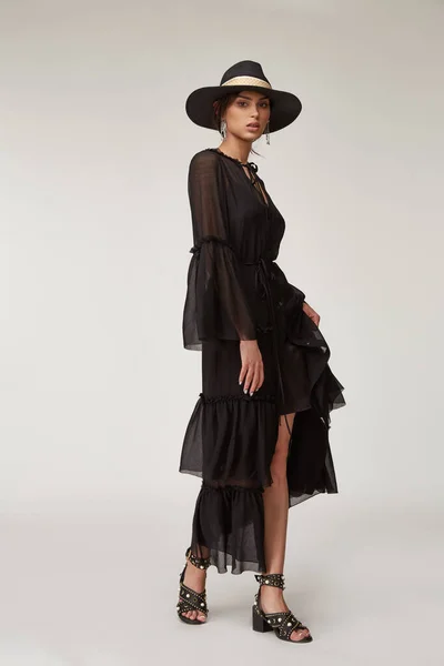 Fashion pretty woman beautiful makeup perfect body shape tan skin wear clothes summer collection organic black cotton cape, silk short dress stylish sandals shoes, accessory hat and jewelry earrings.