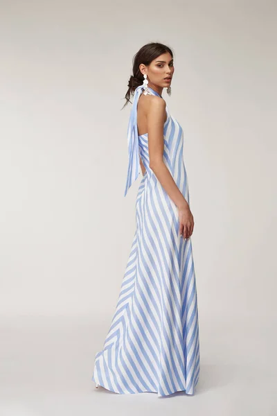 Sexy fashion model beautiful woman pretty face natural makeup, tanned skin body  wear summer collection clothes style for romantic date light silk in white blue stripes long midi dress earrings.